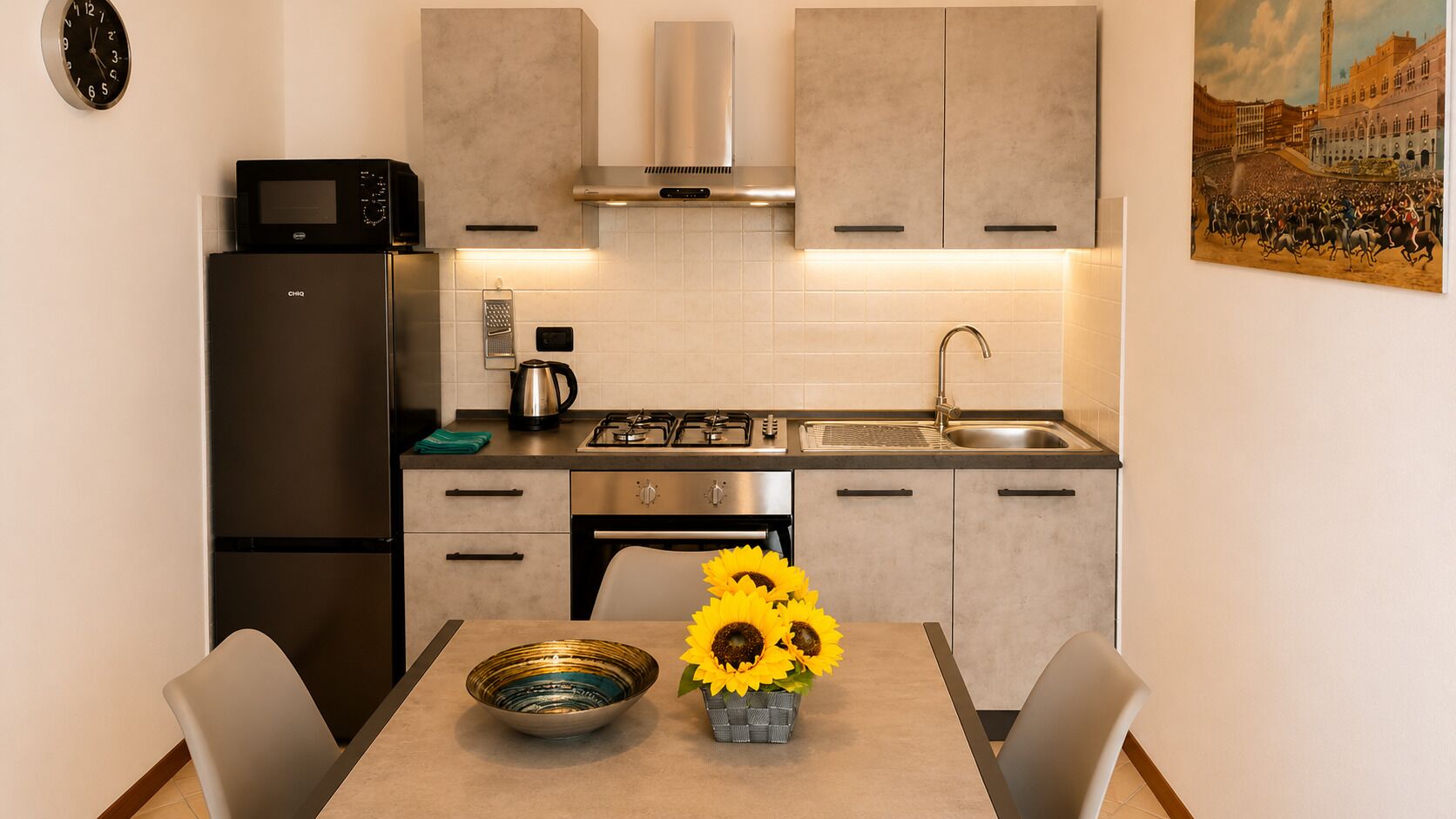 Una cocina moderna con una mesa de comedor, sillas, microondas, tetera y un lavabo.