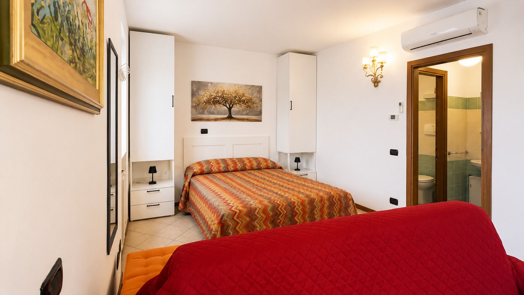 A bedroom with a bed, a nightstand, a dresser, a painting, and an air conditioning unit.