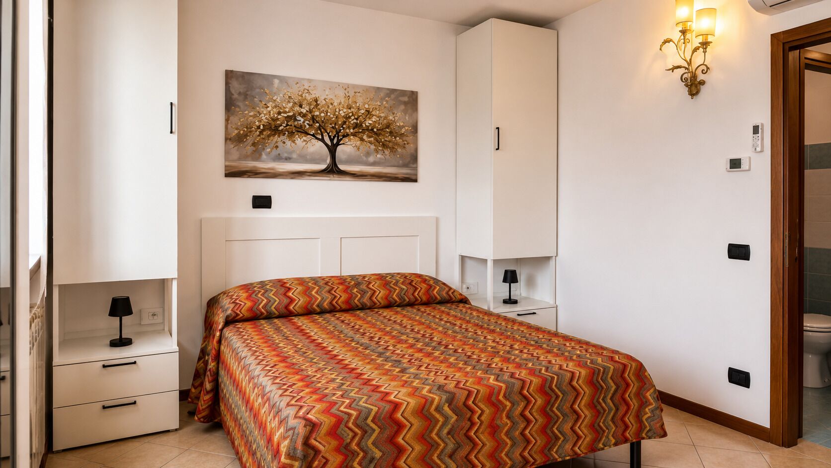 Ein Schlafzimmer mit einem Bett, einem Nachttisch, einer Lampe, einer Wandleuchte, einem Gemälde und einem Kleiderschrank.