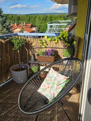 Un balcon avec une chaise, des plantes en pot et une vue sur des maisons et la verdure.
