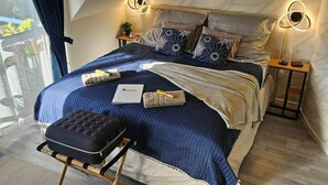 Een slaapkamer met een bed, nachtkastjes, een bankje en uitzicht op het landschap.