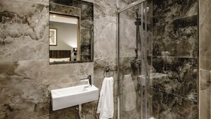 Un baño moderno con pared de mármol, cabina de ducha de vidrio y lavamanos blanco.