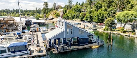 A docked houseboat with a deck and a small boat, surrounded by water and trees.