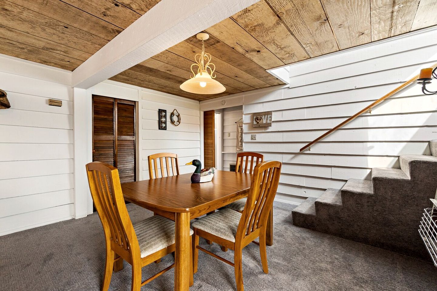 A dining area with a wooden table and chairs, a duck figurine, and a staircase with a wooden handrail.