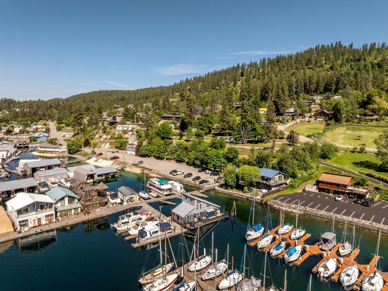 A marina with boats docked, surrounded by residential buildings and a forested hillside.