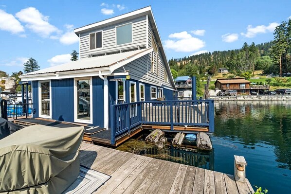 A houseboat with a deck, windows, and a dock extending into a body of water.