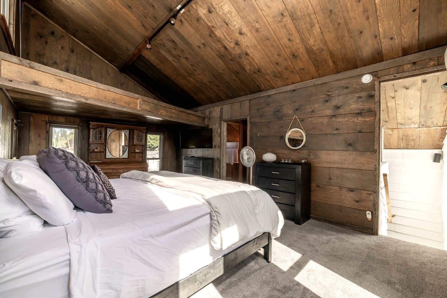 A bedroom with a wooden ceiling, a bed with white bedding, a dresser, and a mirror on the wall.