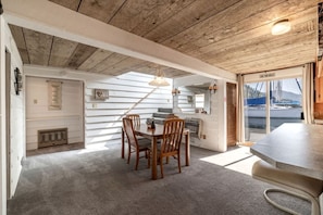 Un comedor con mesa y sillas de madera, una lámpara colgante y vista al agua a través de un ventanal.