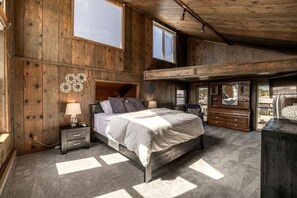 A bedroom with a large bed, a nightstand, a dresser, and a mirror. There is a window above the bed and a door leading to another room.
