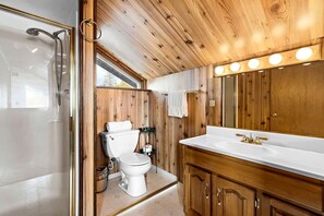 A bathroom with a wooden interior, a shower, a toilet, and a vanity with a mirror.