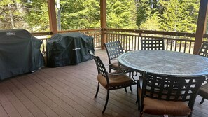 Une terrasse extérieure avec une table ronde et des chaises, un barbecue couvert et une vue sur les arbres.