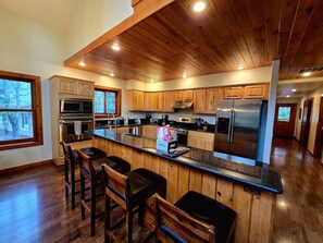 A modern kitchen with wooden cabinets, stainless steel appliances, and a bar area with stools. - Stylish Mountain Retreat with Game Room & Private Fire Pit in McCall, Idaho (McCall)