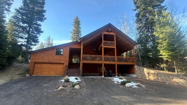 Une cabane en bois à deux étages, dotée d’un balcon, d’un garage et d’un mur de soutènement en pierre.