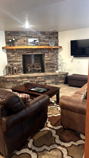 A living room with a stone fireplace, leather sofas, and a flat-screen TV mounted on the wall. - Stylish Mountain Retreat with Game Room & Private Fire Pit in McCall, Idaho (McCall)