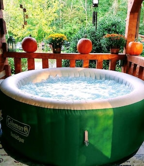 Ein grüner Coleman-Whirlpool auf einer Holzterrasse mit Geländer, umgeben von Herbstlaub und Kürbissen.
