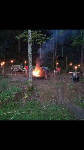 Een kampvuur met stoelen en tafels eromheen, gelegen in een bos.
