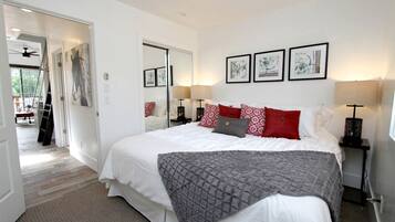 A bedroom with a bed, bedside lamps, a mirror, and artwork on the wall.