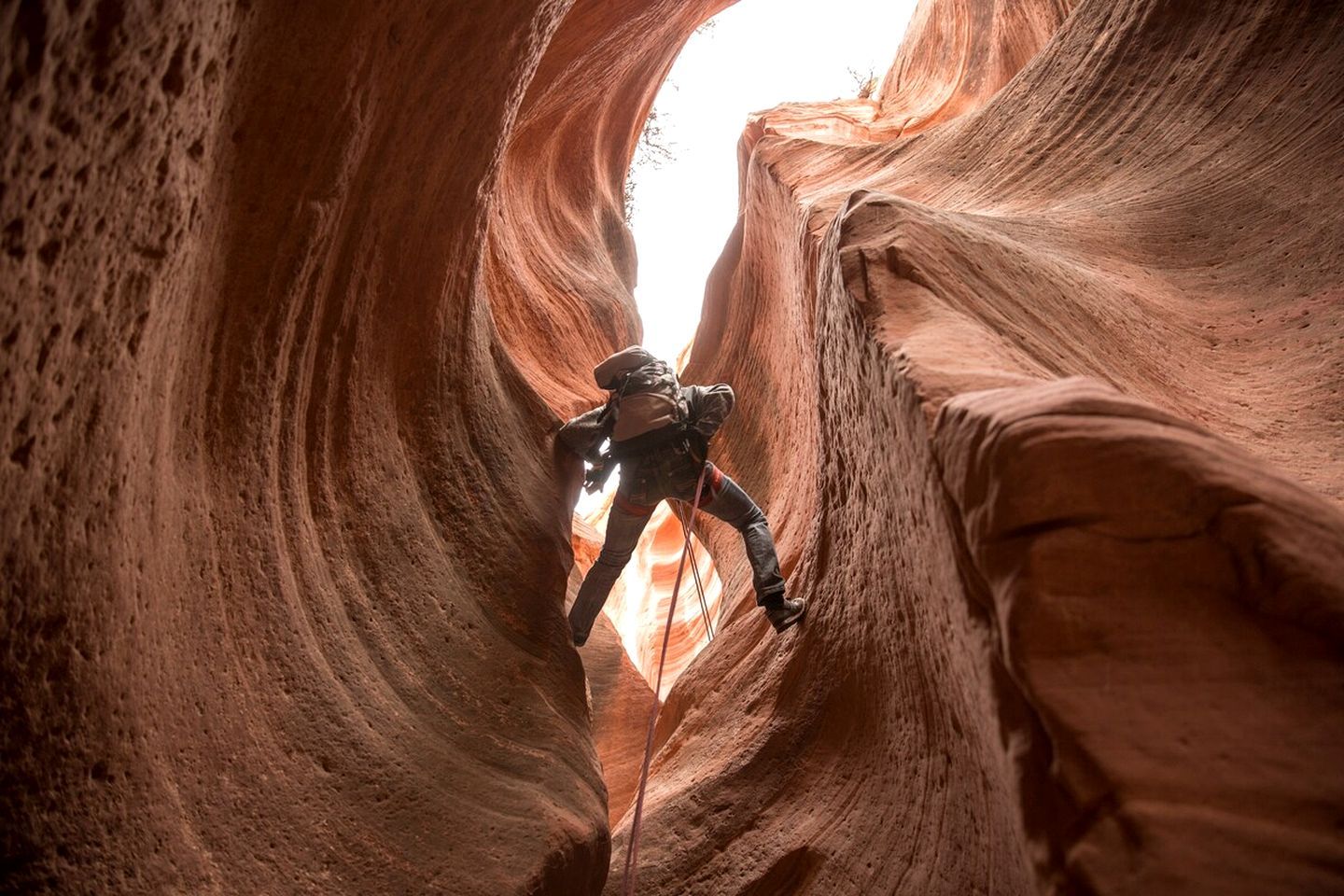 A person climbing a narrow canyon with a bright light at the end.