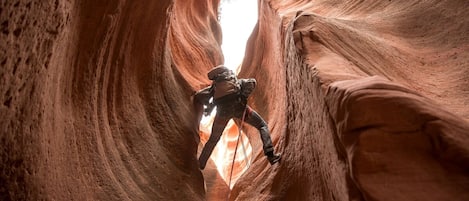 A person climbing a narrow canyon with a bright light at the end.