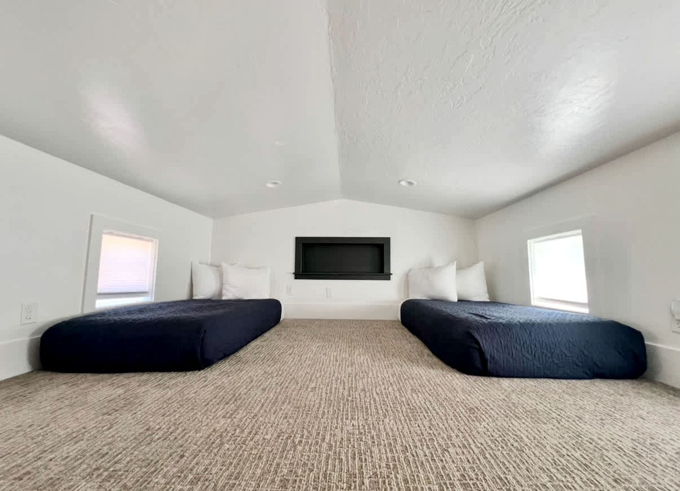 A room with two beds, a large window, and a flat-screen TV mounted on the wall.