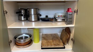 A kitchen cabinet with stainless steel pots, a wooden cutting board, a metal bowl, and a yellow water bottle.