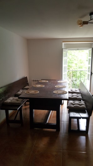 A dining area with a rectangular table, benches, and a view of greenery through a door.