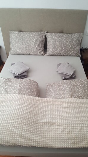 Un lit avec une tête de lit de couleur beige, deux oreillers à motifs floraux et deux serviettes pliées.