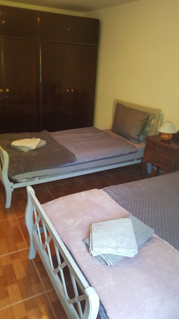A bedroom with two beds, a wardrobe, a nightstand, and a lamp.