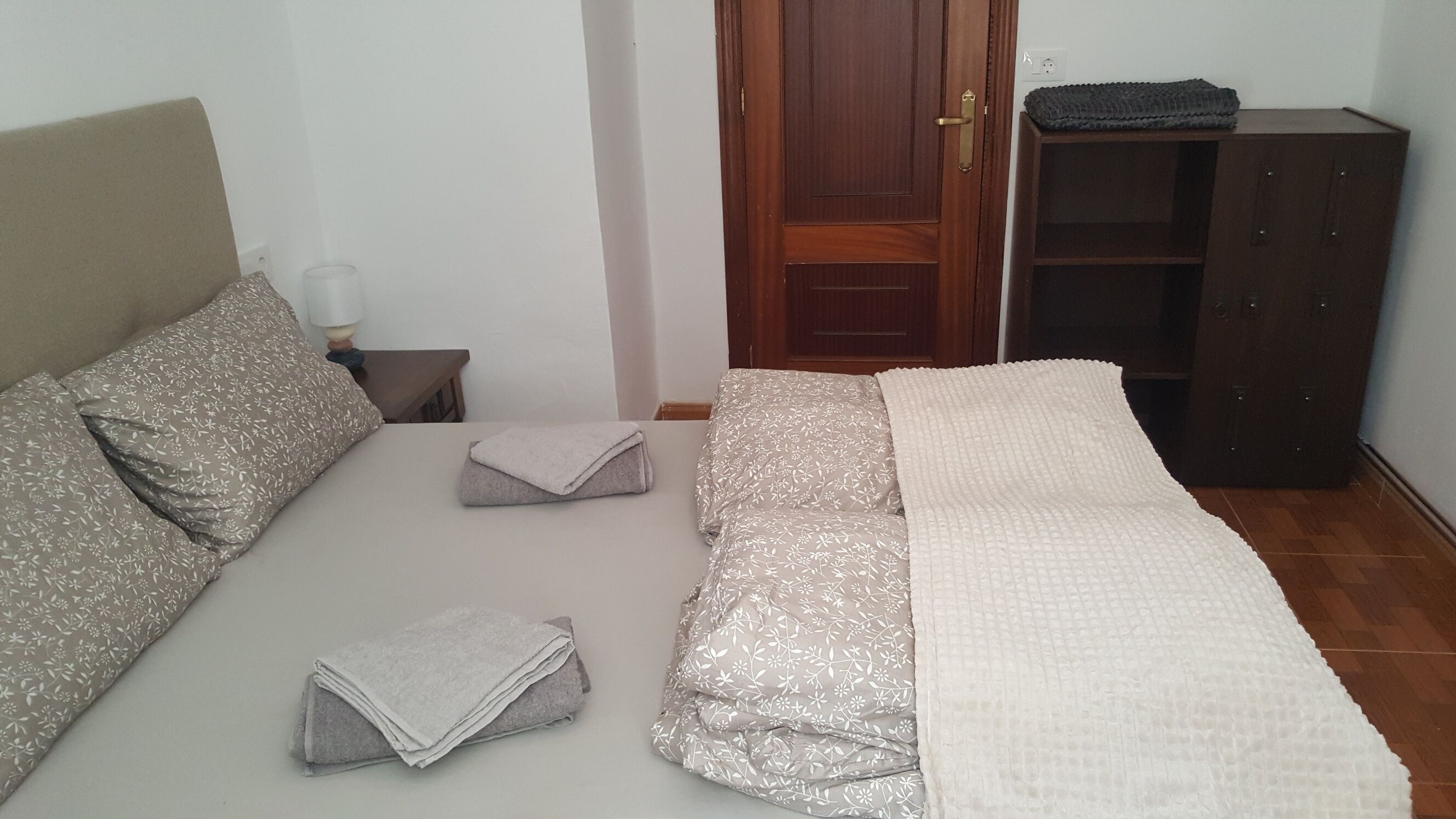 Un dormitorio con cama, almohadas, una mesita de noche con lámpara, un armario y una puerta.