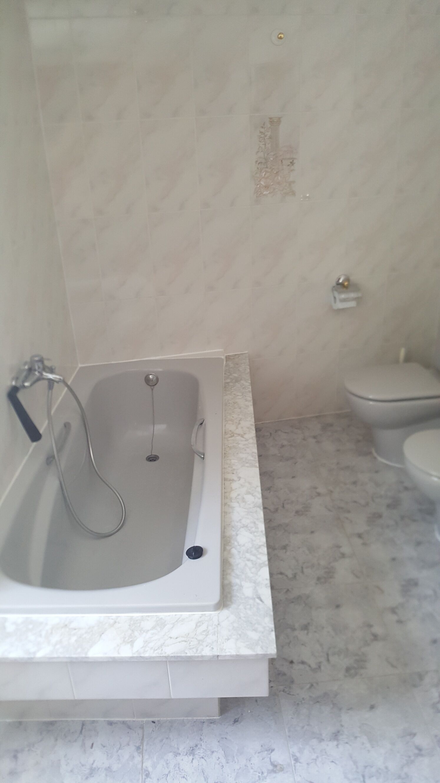 A bathroom with a bathtub, toilet, and marble flooring.