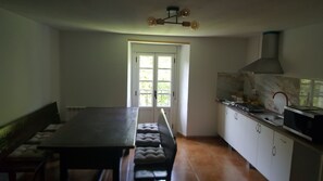 A kitchen with a dining table and bench, a stove, and a window with a view of greenery.