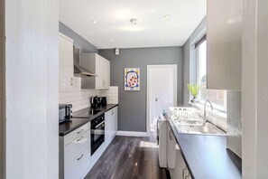 A modern kitchen with white cabinets, a black countertop, and a stainless steel sink. - Central 4-bed home in Kettering by Renzo, Ideal for Contractors, Close to Hospital (Kettering)