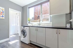 A modern kitchen with a built-in washer, a window with a view of a brick building, and a door leading to another room. - Central 4-bed home in Kettering by Renzo, Ideal for Contractors, Close to Hospital (Kettering)