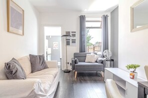 A modern living room with a sofa, armchair, and a small table with a plant. - Central 4-bed home in Kettering by Renzo, Ideal for Contractors, Close to Hospital (Kettering)