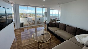 Ein modernes Wohnzimmer mit großem Fenster, einer Couch, einem Glastisch und einem Essbereich.