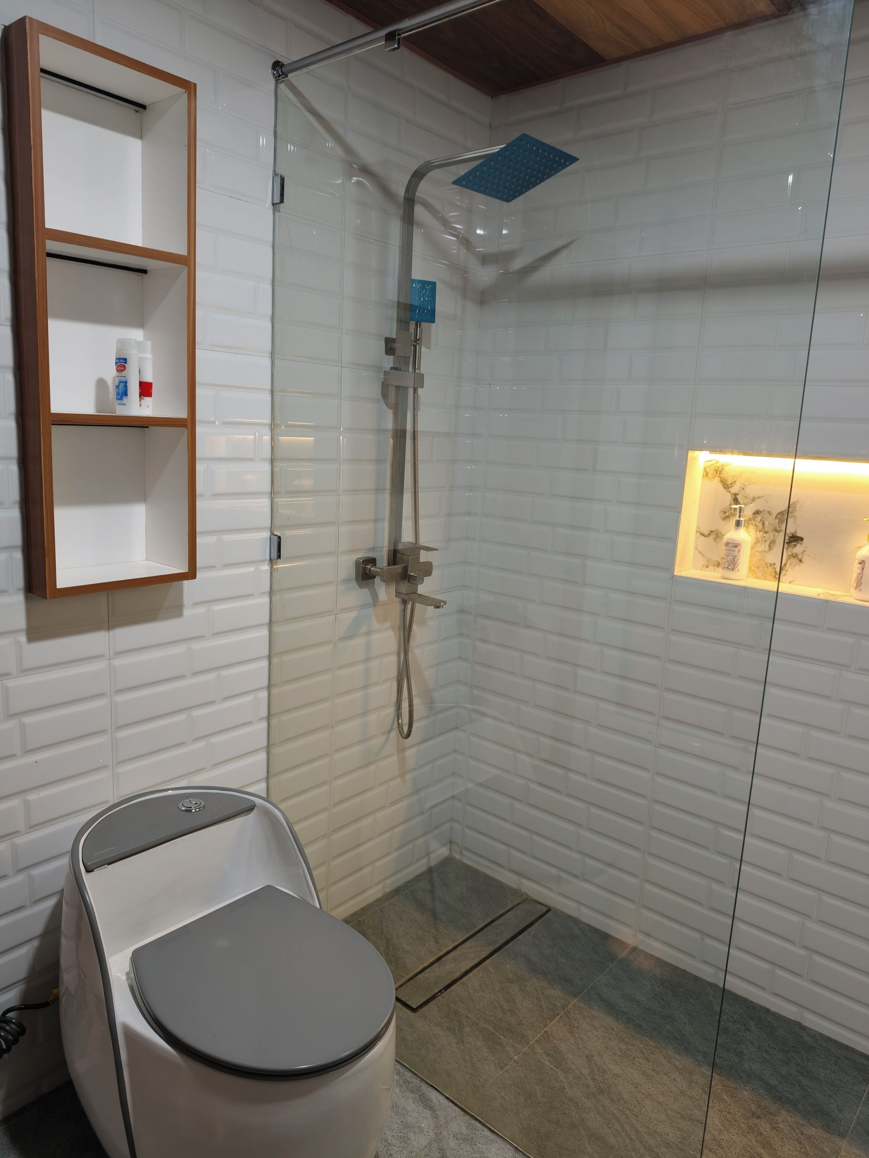 A modern bathroom with a glass-enclosed shower, a toilet, and a shelf with toiletries.