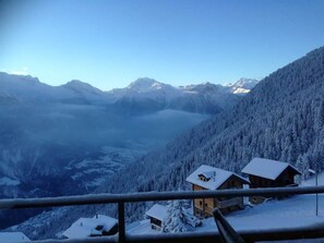A mountain cabin with a view of a valley and snow-covered trees.