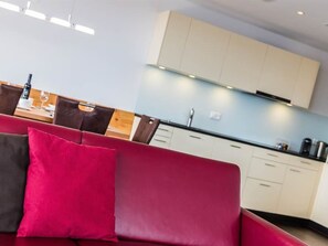 Eine moderne Küche mit hellen Schränken und einem roten Sofa mit Kissen.
