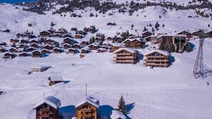 Un complejo turístico en la montaña cubierto de nieve, con varias cabañas de madera, pistas de esquí y un telesilla.