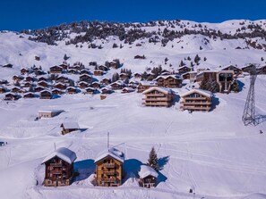 Ein verschneiter Bergort mit mehreren Holzgebäuden, Skipisten und einer Seilbahn.