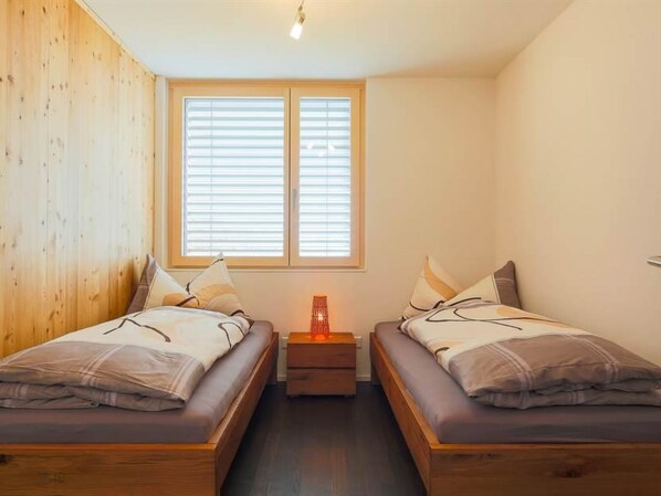 A room with two beds, a nightstand, and a window with blinds.