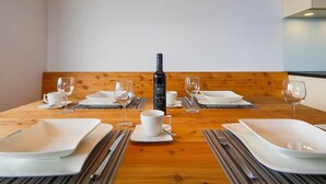 Mesa de comedor para cuatro personas, con platos blancos, cubiertos y vasos, y una botella de vino en el centro.