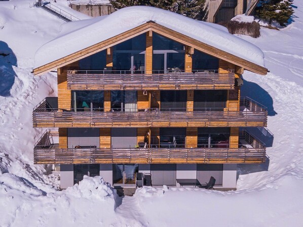 A multi-story wooden chalet with balconies, set in a snowy landscape.