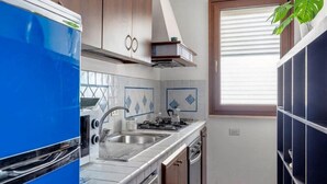 A compact kitchen with a blue refrigerator, a gas stove, a sink, and wooden cabinets. - Mondello Bay - Addaura Apartments (Palermo)