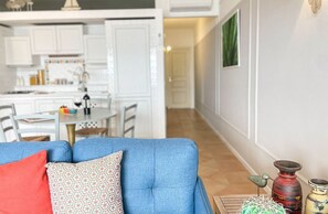 Ein Wohnzimmer mit blauem Sofa, einem Essbereich mit Tisch und Stühlen sowie einer Küche im Hintergrund.