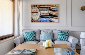 A living room with a grey sofa, patterned cushions, a coffee table with candles, and a framed picture on the wall. - Mondello Bay - Addaura Apartments (Palermo)