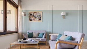 A living room with a sofa, armchair, coffee table, and a painting on the wall. - Mondello Bay - Addaura Apartments (Palermo)
