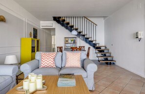 Ein Wohnzimmer mit einem grauen Sofa, einem Couchtisch mit Kerzen, einem gelben Schrank und einer Treppe mit blauer Geländer.