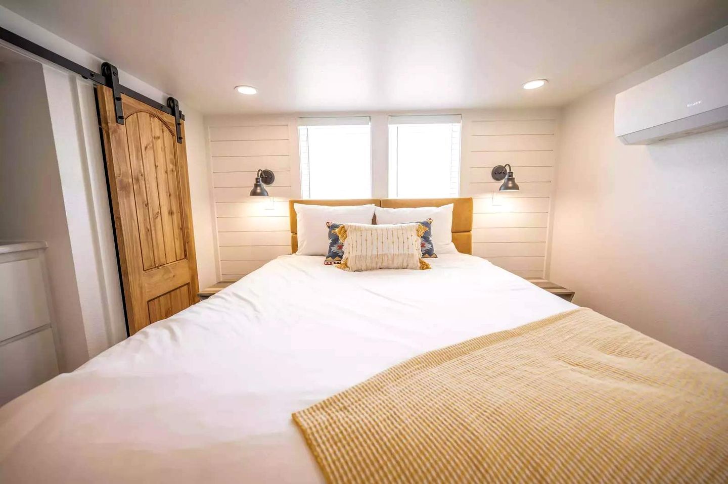 A bedroom with a bed, two bedside lamps, a wooden door, and a window.