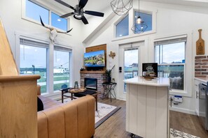 A spacious living room with a fireplace, a television, and a large window overlooking a scenic view. - Serene Tiny Home Retreat with Resort Amenities Near Fredericksburg, TX (Fredericksburg)